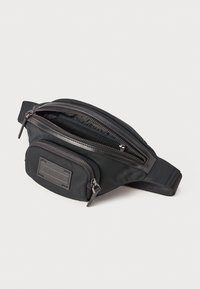 Mala de cintura preta em nylon com uma textura suave, apresentando múltiplos compartimentos com fecho e um patch de логотип em relevo na frente.