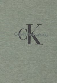 Ljusgrön bomulls-t-shirt med en stor svart "CK" logotyp och texten "Calvin Klein Jeans" under i grått. Mjuk, strukturerad tyg.