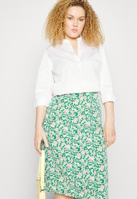 Camisa branca de colarinho, com botões, e mangas arregaçadas, combinada com uma saia lápis floral verde com flores rosa e brancas.