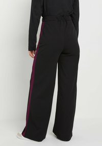 Pantaloni neri a gamba larga con vita elastica e strisce laterali color porpora, realizzati in un tessuto morbido, caratterizzati da una texture liscia e una vestibilità comoda.