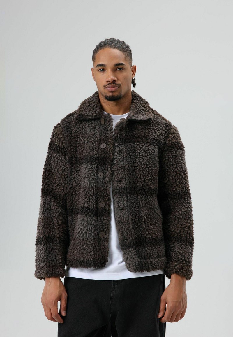 Brown fur jacket with a textured, shaggy finish; button-up front; a collared neck; cropped design; worn over a white shirt.
