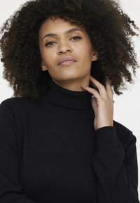 Pull noir à col roulé avec un col et des poignets côtelés, texture douce, design ajusté et manches longues. Pas de motifs ni de matériel visible.