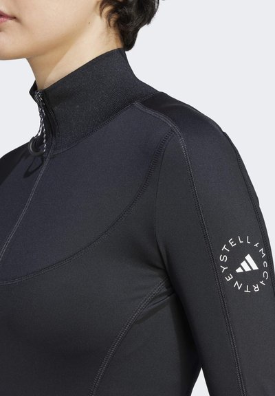 Top atlético negro con cuello alto, cierre de cremallera y detalles de costura. Presenta un logotipo en el brazo izquierdo y un diseño ajustado.
