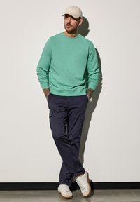 Ljusgrön sweatshirt, marinblå cargobyxor och vita sneakers. Avslappnad design med ribbad manschett och fickor på byxorna.