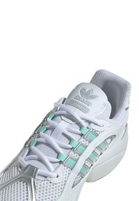 Bijele mrežaste sportske cipele sa srebrnim detaljima i mint zelenim elementima. Imaju podstavljeni ovratnik i teksturirani potplat za poboljšano prianjanje.