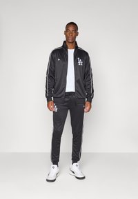 Black athletic track suit with white stripes, featuring a zip-up jacket and tapered pants. The logo "LA" is prominently displayed on both pieces.