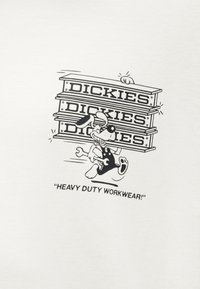 Κινούμενος σκύλος σε φόρμες που κουβαλά τρεις στοιβαγμένες ατσάλινες δοκούς με την ετικέτα "DICKIES" και ένα γερμανοπολύγωνο, με λεζάντα "ΕΡΓΑΣΙΑΚΑ ΡΟΥΧΑ ΓΙΑ ΒΑΡΙΑ ΧΡΗΣΗ!"