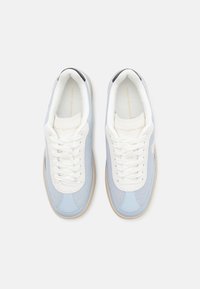 Baskets en cuir bleu clair et blanc, texture perforée, lacets plats et branding discret sur la languette et le côté.