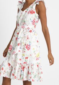 Weißes Blumenkleid mit mehrfarbigen Blumenmustern, Rüschenträgern, Taillierung und gerafftem Saum. Leichter, sommerlicher Stoff.