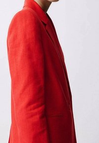 Blazer en lin rouge à coupe ajustée, fermeture simple à bouton, revers en encoche et poche latérale. Texture lisse avec un minimum de détails.