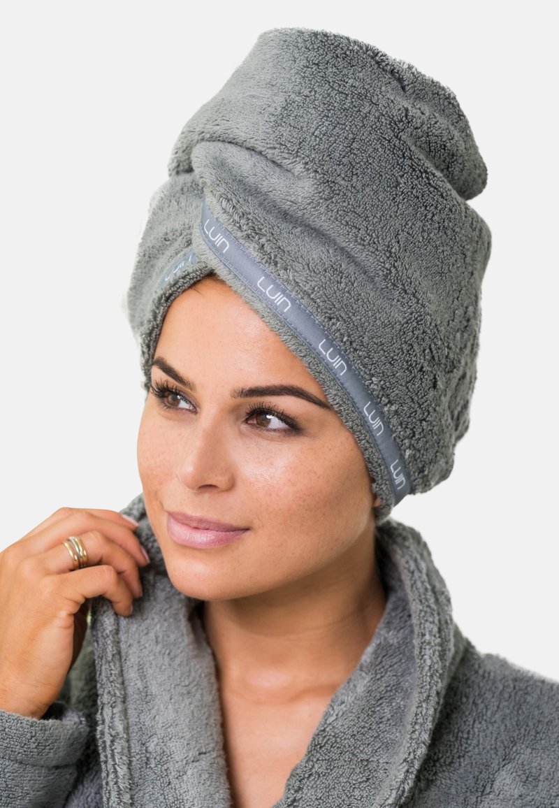Pilkas, pūkuotas turbanas rankšluostis su tekstūruota paviršiumi ir pilka juosta, pažymėta "Luin". Minkštas ir sugeriantis, sukurtas plaukų džiovinimui.
