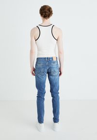 Blå denimjeans med smal passform, med en läderlapp på midjebandet och böjd sömmar på bakfickorna. Kombinerat med en vit linne.