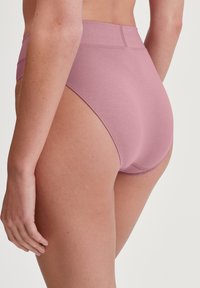 Sous-vêtements taille haute en tissu rose doux, présentant une texture lisse et des détails de couture minimaux le long de la taille et des ouvertures de jambes.