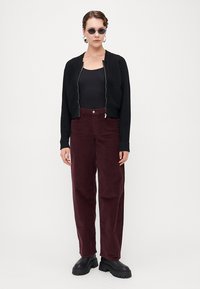 Svart zip-up kofta, åtsittande svart bodysuit, vinröda vida corduroy-byxor och tunga svarta plattformskor. Solglasögon och örhängen ingår.