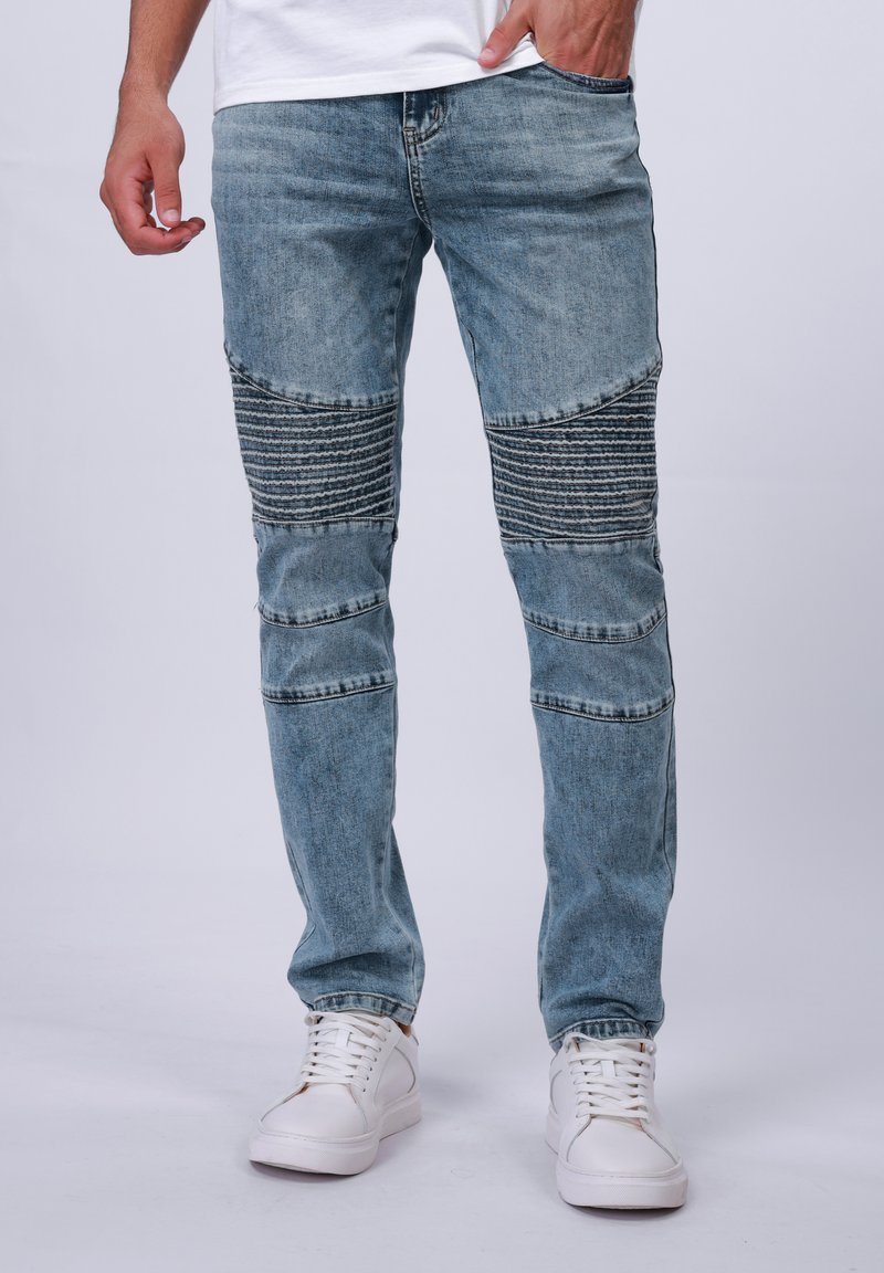 Jeans de mezclilla de color azul claro con acentos texturizados en las rodillas y detalles a rayas. Presenta un corte clásico con un ligero ajuste en los tobillos.