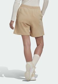 Beżowe szorty z bawełny z elastycznym pasem, kieszeniami bocznymi i luźnym krojem. Noszone z jasnymi butami sportowymi i skarpetkami do kostek.