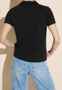 Svart polo t-shirt med korta ärmar, slät tyg, ribbad krage och en figurnära design, i kombination med ljusblå högmidjade jeans.