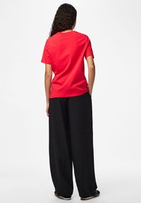 Rød bomuld t-shirt med korte ærmer, der viser en afslappet pasform. Kombineret med løse sorte bukser og slip-on sko.