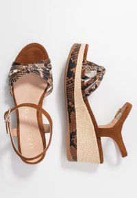 Sandalias de cuña de ante marrón con estampado de serpiente y plataforma de yute trenzado. Cuentan con una correa para el tobillo y un diseño decorativo de crisscross.