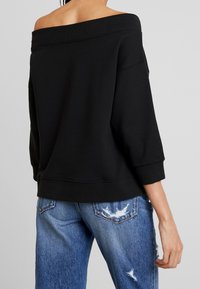 Felpa nera off-the-shoulder con una consistenza morbida e scollatura ampia, abbinata a jeans in denim blu strappati con una vestibilità comoda.