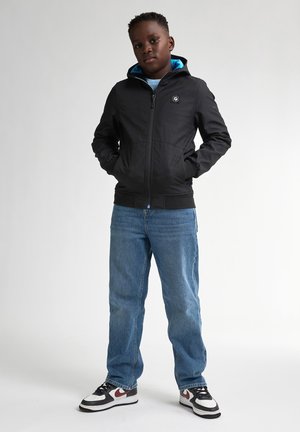 Schwarze Zip-Per-Hoodie mit blauem Innenfutter, mit einem Logo auf der Brust. Kombiniert mit blauen Jeans und Schwarz/Weißen Sneakern.