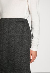 Falda lápiz de mezcla de lana, de longitud a la rodilla, en gris oscuro con un patrón de espiga, combinada con un suéter de punto de color claro.