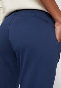 Granatowe spodnie wykonane z miękkiego materiału, o gładkiej fakturze, dopasowanym kroju i bocznych kieszeniach, z dyskretnym detalem w postaci tylnej kieszeni.