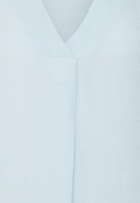 Jasnoniebieska lniana bluzka z dekoltem w serek, z delikatnym szwem na środku, gładką teksturą i luźnym krojem.