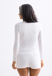 White long-sleeve top made of stretchy fabric, paired with white shorts. Both have a smooth texture and minimal design details.