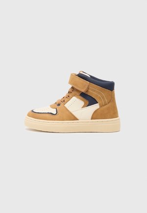 Wysoki sneaker z jasnobrązowym zamszem, kremowymi i granatowymi panelami ze skóry, sznurowaniem z przodu oraz paskiem na rzep na kremowej gumowej podeszwie, widok z boku na jasnoszarym tle.