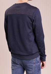 Námořnická modrá mikina s texturovaným tmavě modrým yoke, žebrovanými manžetami a lemem. Měkká tkanina, volný střih a minimalistický design.