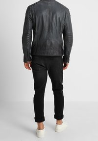 Svart läderjacka med kviltade axel- och armbågsdetaljer, kombinerad med svarta jeans och vita sneakers. Bakvy visar en skräddarsydd design.