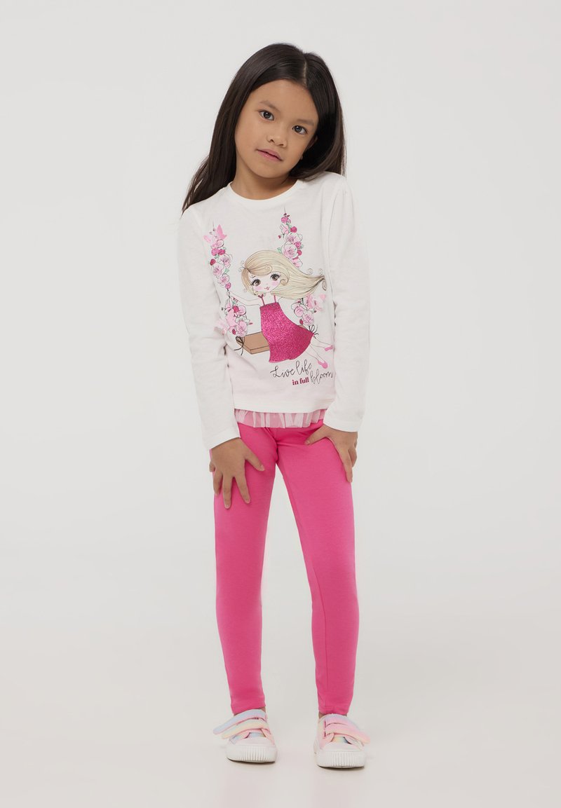 Camicia bianca a maniche lunghe con un design colorato di una ragazza stampato, abbinata a leggings fucsia e sneakers bianche con accenti pastello.