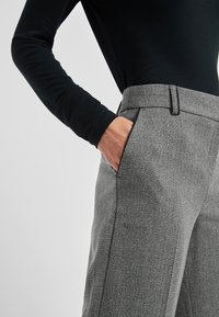 Grijze wollen broek met een getailleerde pasvorm, voorzien van een platte voorkant, zijzakken en een gladde textuur. Gepaard met een zwart langslief top.