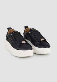 Sneaker in pelle nera con suola piatta in gomma bianca, punta rotonda, design con lacci e dettagli di branding discreti sul lato.