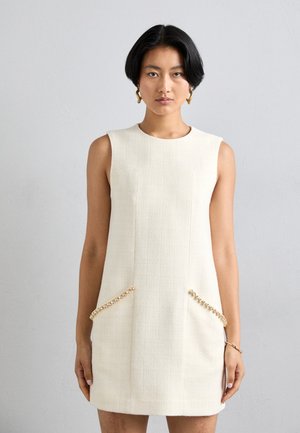 Ärmelloses, cremefarbenes Kleid aus strukturiertem Stoff mit zwei Fronttaschen, die mit goldenen Perlenakzenten verziert sind. Schlichtes, rundes Dekolleté.