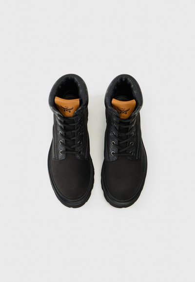 Chaussures montantes en cuir noir avec col rembourré, bout rond et lacets noirs. Présentent un accent beige au niveau de la languette et des semelles en caoutchouc.