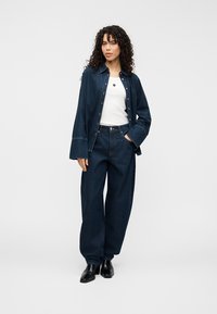 Τζιν μπουφάν και φαρδιά τζιν σε σκούρο μπλε. Λευκό t-shirt από μέσα. Μαύρα μπότες αστραγάλου. Λεία υφή, μπροστινό μέρος με κουμπιά στο μπουφάν.