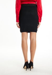 Zwarte kokerrok met een gestructureerde tailleband. G gedragen met een rode blouse en zwarte hoge hakken. Glad materiaal, aansluitend ontwerp, tot de knie.