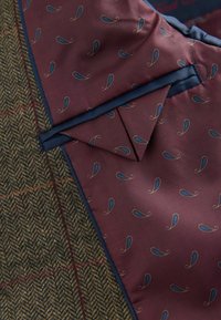 Brun tweed-stof med rødt og grønt ternmønster ved siden af mørkerød silke med blå paisley-print og blå stofkant.