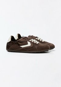 Paire de baskets basses marron décontractées avec des lacets blancs, des renforts au talon blancs et un motif blanc en forme de chevron sur les côtés.