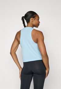 Lichtblauw sporttop met een racerback ontwerp, gemaakt van een gladde, elastische stof. Gepaard met zwarte leggings.