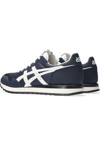 Navy blue athletic sneakers with white accents, fabric and synthetic upper, textured sole, low-profile design, and branded heel.