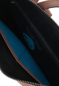 Borsa in pelle marrone con un interno nero, dotata di una tasca con zip, foderata con un tessuto blu brillante e con cuciture rinforzate.