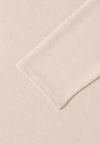 Beige ribbat tyg med närbild av en lång ärm vikt diagonalt över klädesplagget.