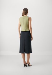 Ärmlös grön topp i kombination med en knä-lång svart kjol med en slits bak. Slät textur, figurnära design och minimalistisk stil.