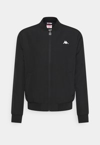 Giacca bomber nera con superficie testurizzata, zip frontale, polsini e orlo a coste, e un logo bianco sul lato sinistro del petto. Etichetta di misura media all'interno.