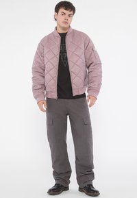 Light pink quilted bomber jacket with a ribbed collar, paired with dark gray cargo pants featuring multiple pockets and black shoes.