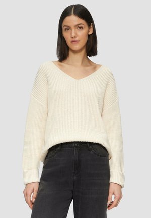 V-neck knitted sweater in cream with a loose fit, textured fabric, and ribbed cuffs, paired with black jeans.