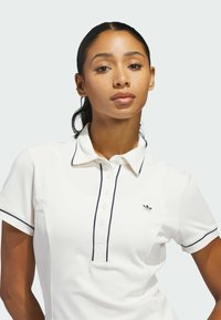 Weißes Polohemd mit marineblauen Akzenten, Knopfleiste und gesticktem Logo auf der linken Brustseite. Hergestellt aus einem strukturierten Stoff für Komfort.